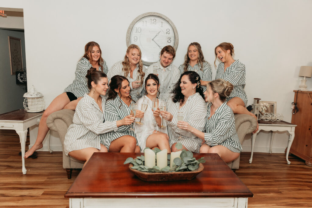 Bride sitting with her bridesmaids during wedding morning getting ready, sharing drinks and laughing together before the ceremony.